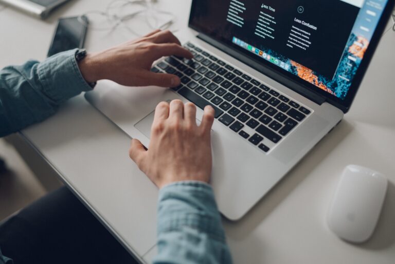Laptop on a desk with mans hands and forarms on the keyboard providing website support